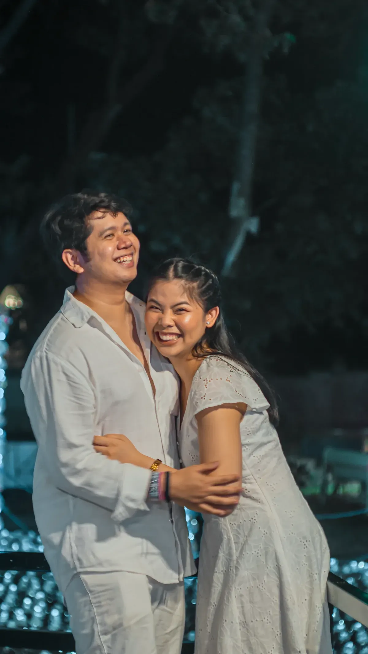 Tommy and Jeyan laughing together, dressed in white among soft lights