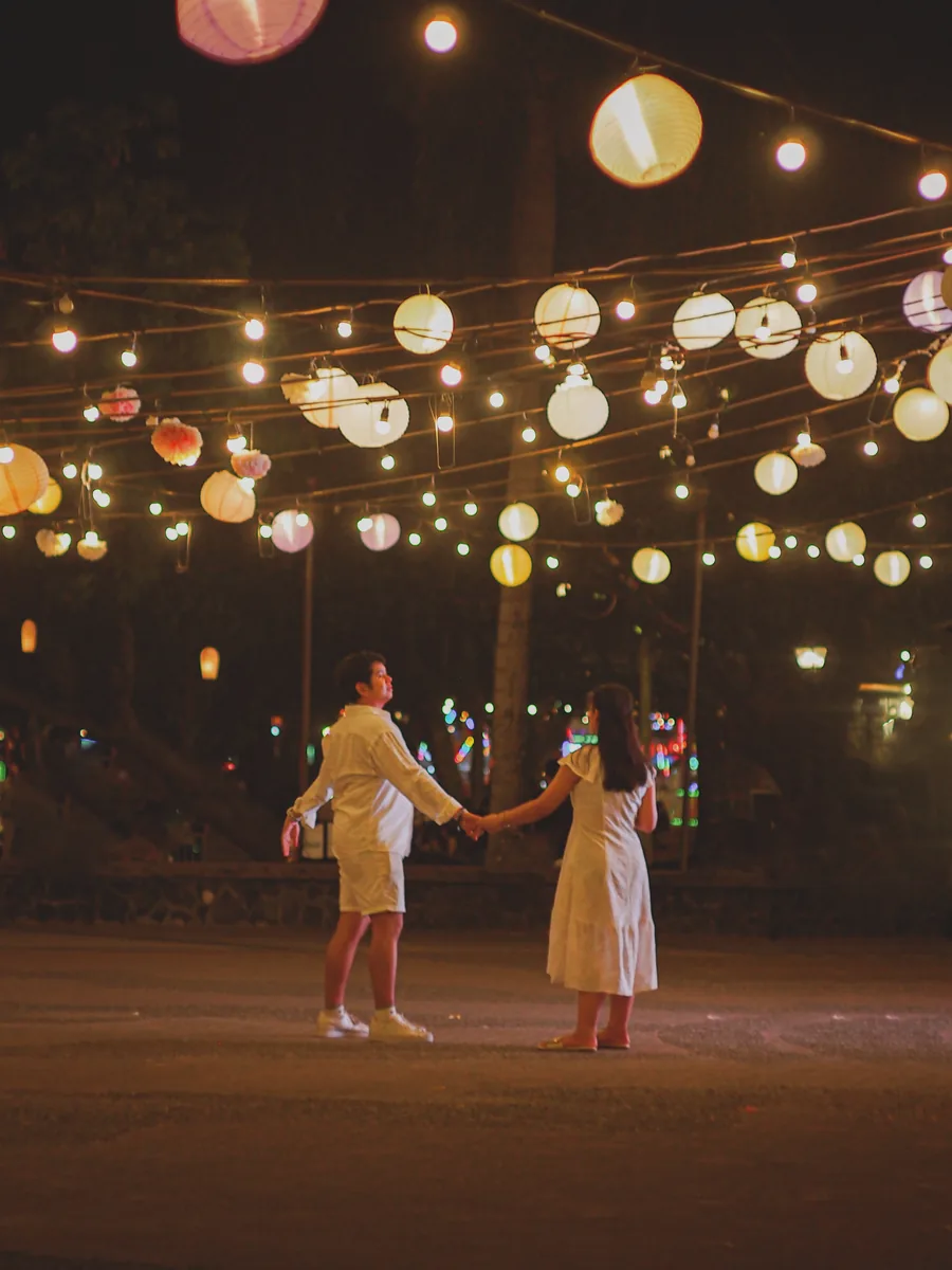 Tommy and Jeyan holding hands beneath strings of glowing paper lanterns