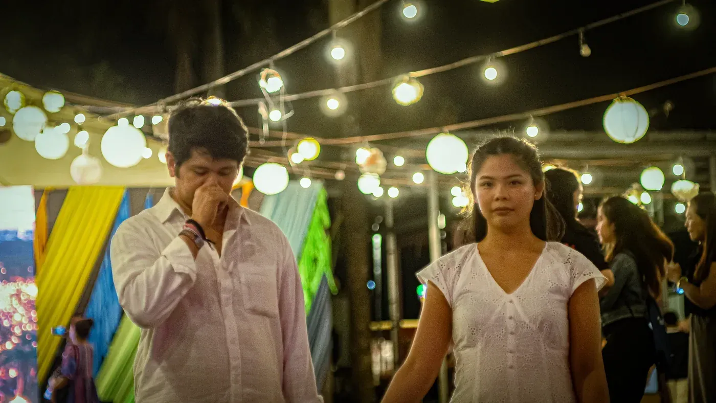 Tommy and Jeyan beneath strings of warm festival lights at dusk